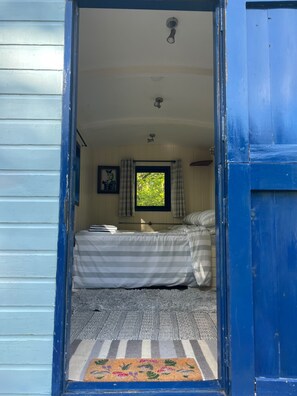Una habitación con cama, ventana con cortinas, ventilador de techo y puerta.