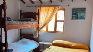 Ein Zimmer mit zwei Etagenbetten, einem Einzelbett, einem kleinen Tisch, einem Stuhl und einem Fenster mit Vorhängen.