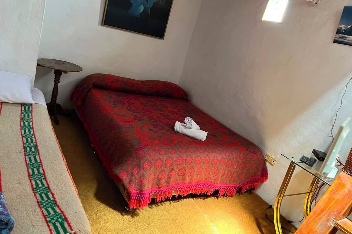 Una habitación con una cama, una mesita pequeña, una silla y un cuadro en la pared.