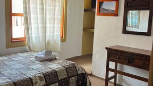 Ein Schlafzimmer mit einem Bett, einer Holzkommode, einem Spiegel und einem Fenster mit Vorhängen.