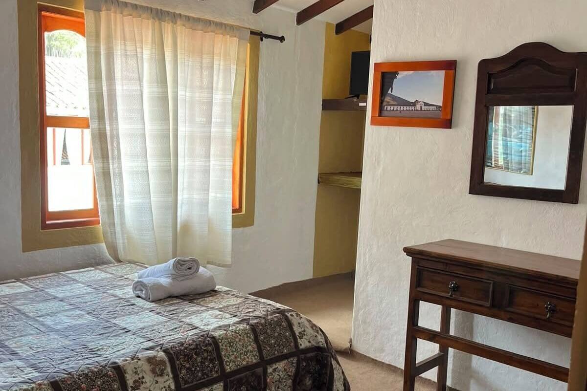 Un dormitorio con una cama, un aparador de madera, un espejo y una ventana con cortinas.