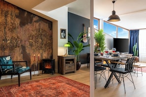 Ein modernes Wohnzimmer mit Kamin, einer Essecke mit Tisch für zwei Personen und einem großen Fenster mit Blick.
