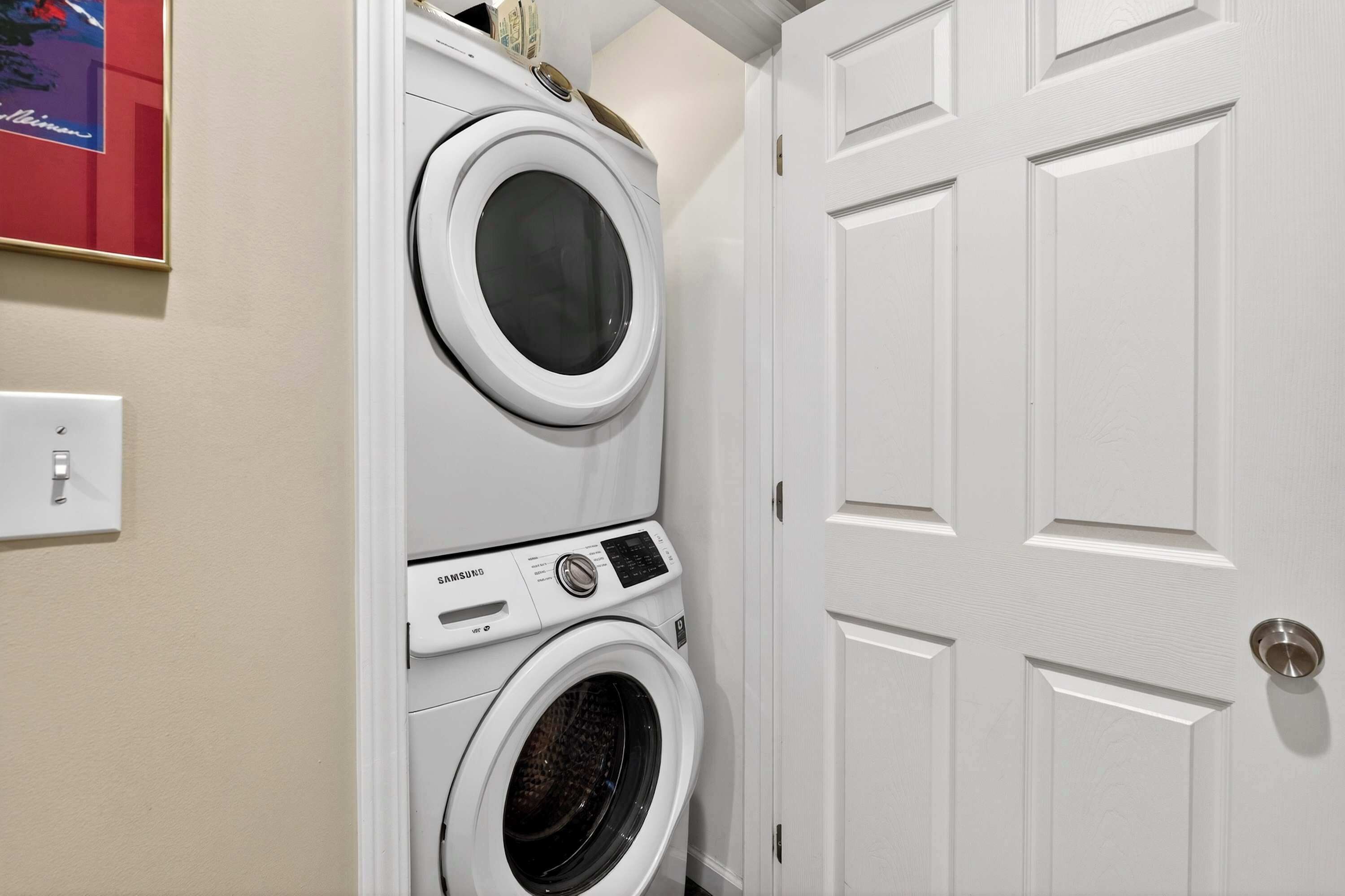 A laundry area with stacked washers and dryers, a door, and a light switch.