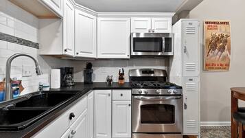Une cuisine avec des meubles blancs, une cuisinière en acier inoxydable, un four à micro-ondes et un réfrigérateur.