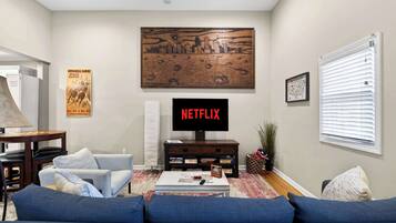 A living room with a TV, sofa, coffee table, and a cityscape painting.