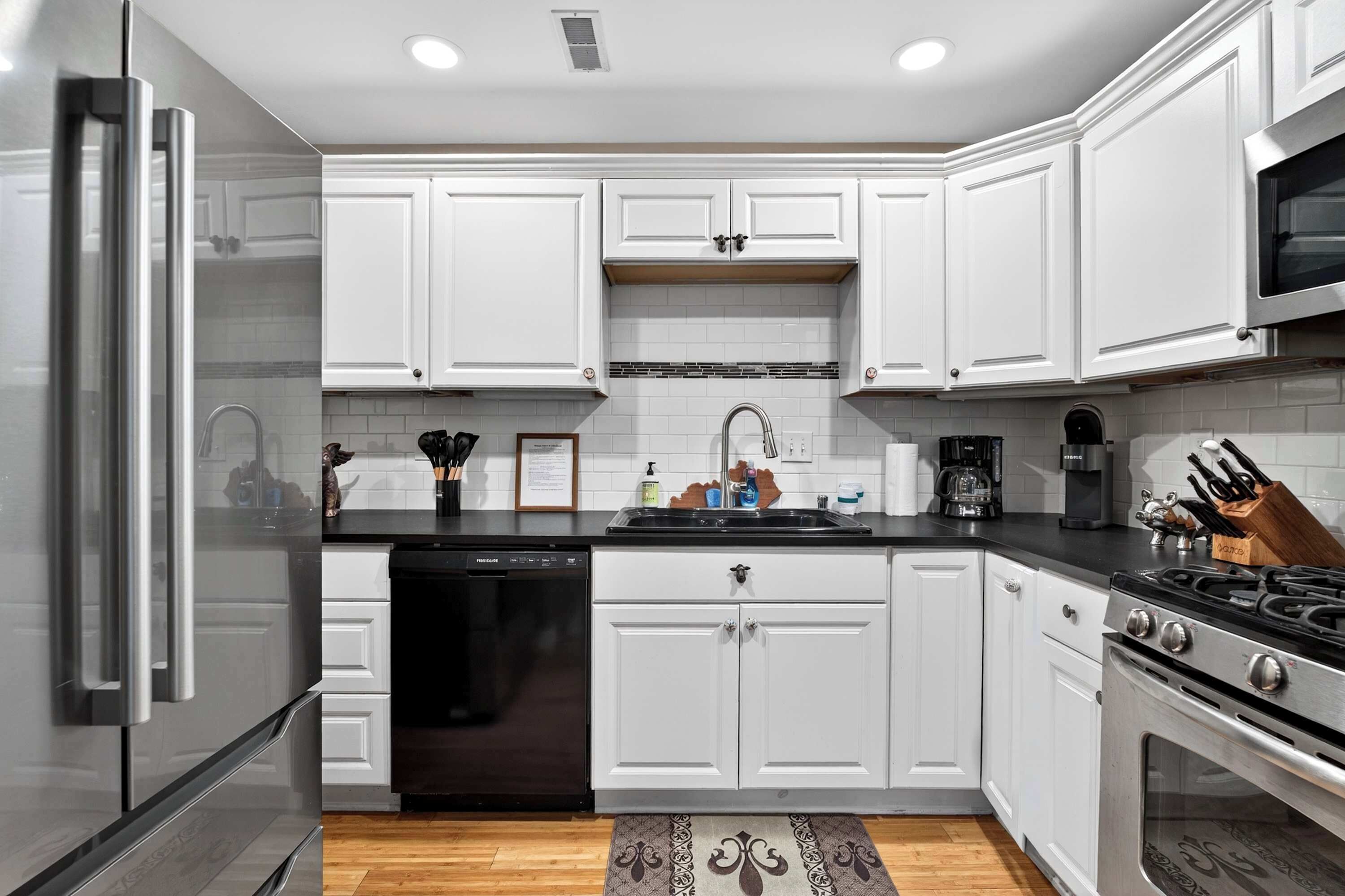 Una cocina moderna con armarios blancos, un refrigerador de acero inoxidable, un lavavajillas, una estufa y un microondas.