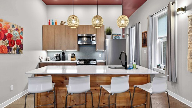 Una cocina moderna con una isla central, taburetes de bar, lámparas colgantes y un amplio ventanal con cortinas.
