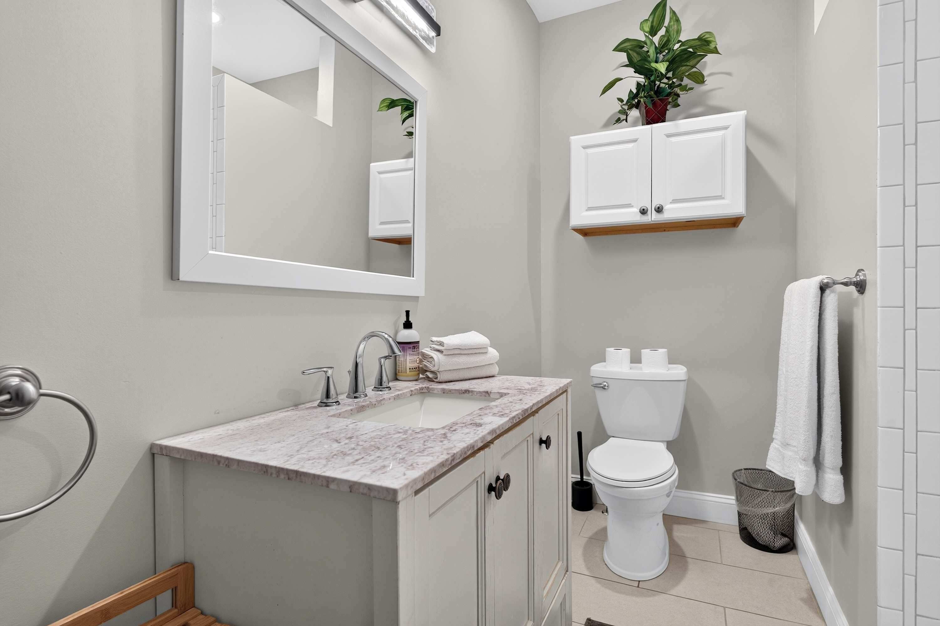 A modern bathroom with a marble sink, a toilet, a mirror, and a potted plant.