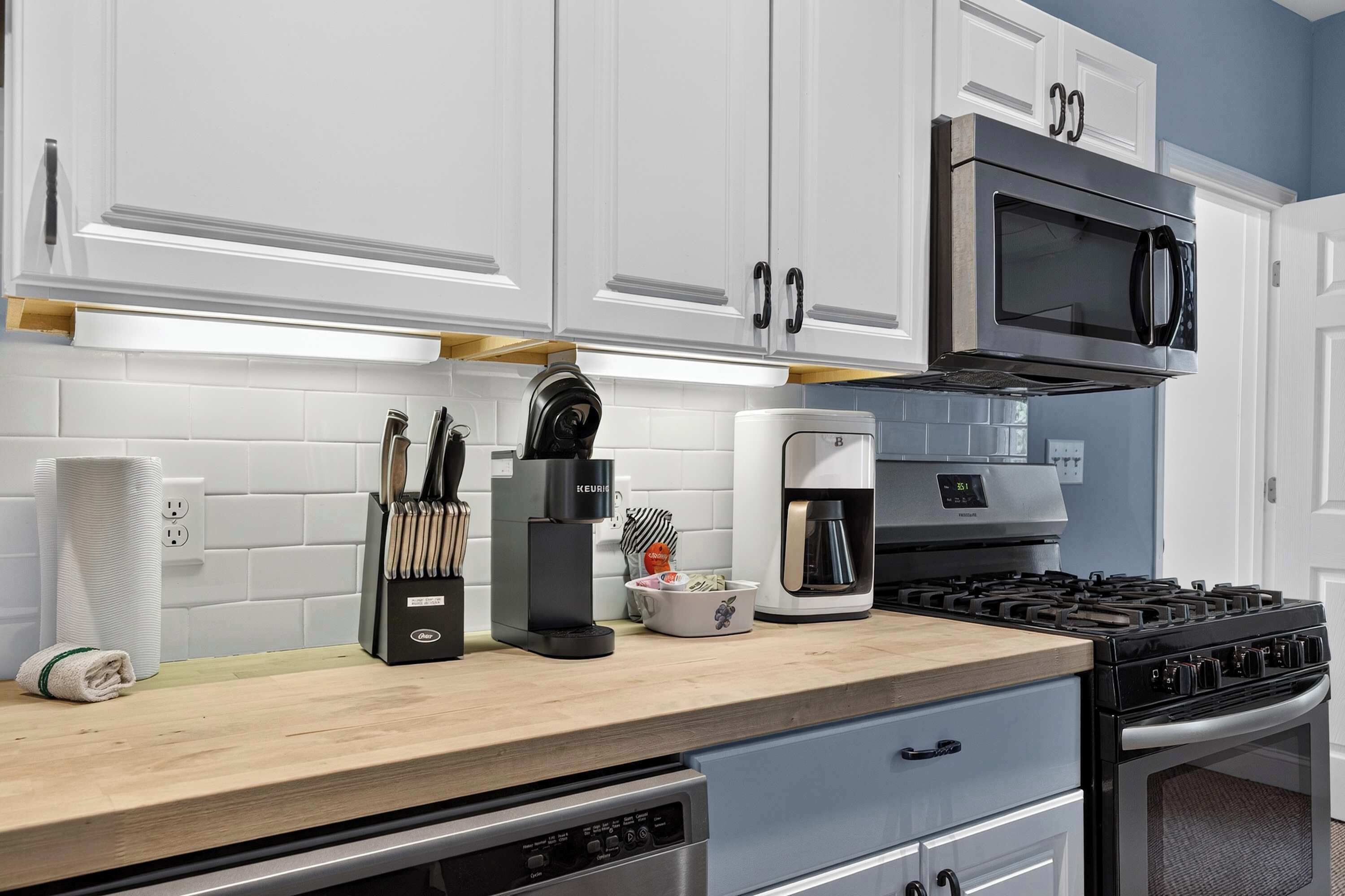 A modern kitchen with white cabinets, a built-in microwave, a coffee maker, and a gas stove.