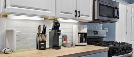 A modern kitchen with white cabinets, a built-in microwave, a coffee maker, and a gas stove.
