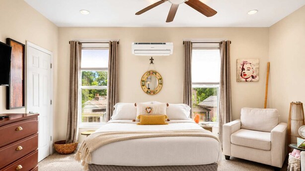 Un dormitorio con una cama, una silla, un ventilador de techo y un aire acondicionado.