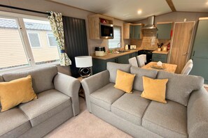 Ein kompakter Wohnbereich mit zwei grauen Sofas, einem kleinen Tisch, einem Fernseher und einer Küchenzeile.