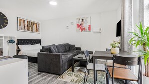 Een moderne, goed verlichte kamer met een bed, grijze bank, eettafel, stoelen, een televisie en kunstwerken aan de wanden.