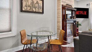 A dining area with a glass table and leather chairs, a fireplace with a Netflix sign, and a framed horse painting on the wall. - Spacious and cozy Highlands unit near attractions! (Louisville)