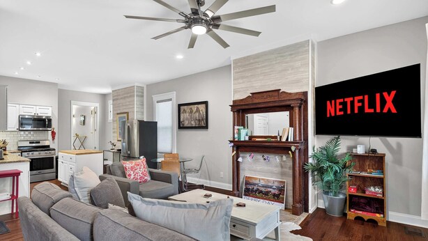 A modern living room with a sofa, coffee table, fireplace, television, and a kitchen area in the background. - Spacious and cozy Highlands unit near attractions! (Louisville)
