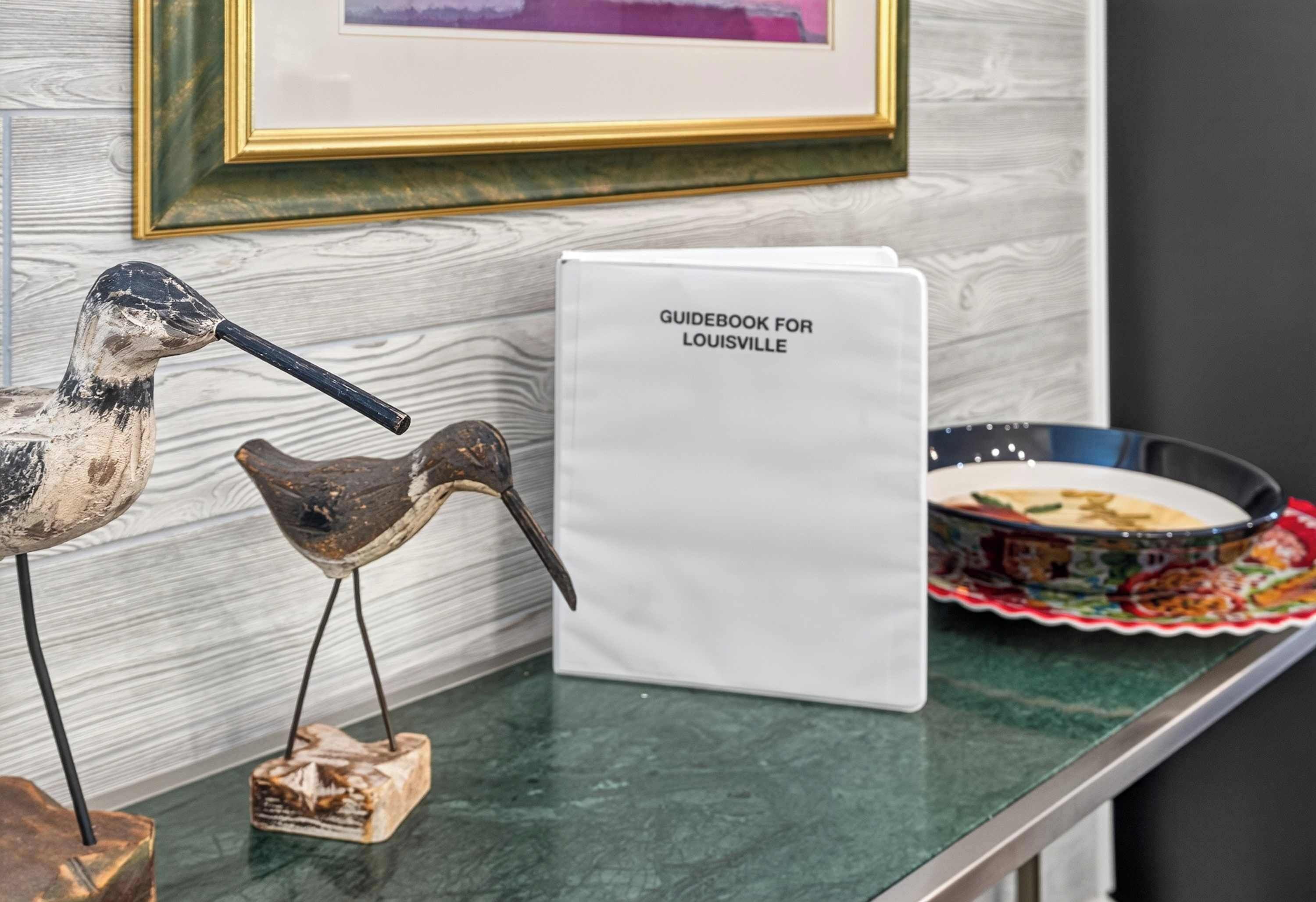 A guidebook for Louisville on a counter, a bird sculpture, and a decorative bowl.