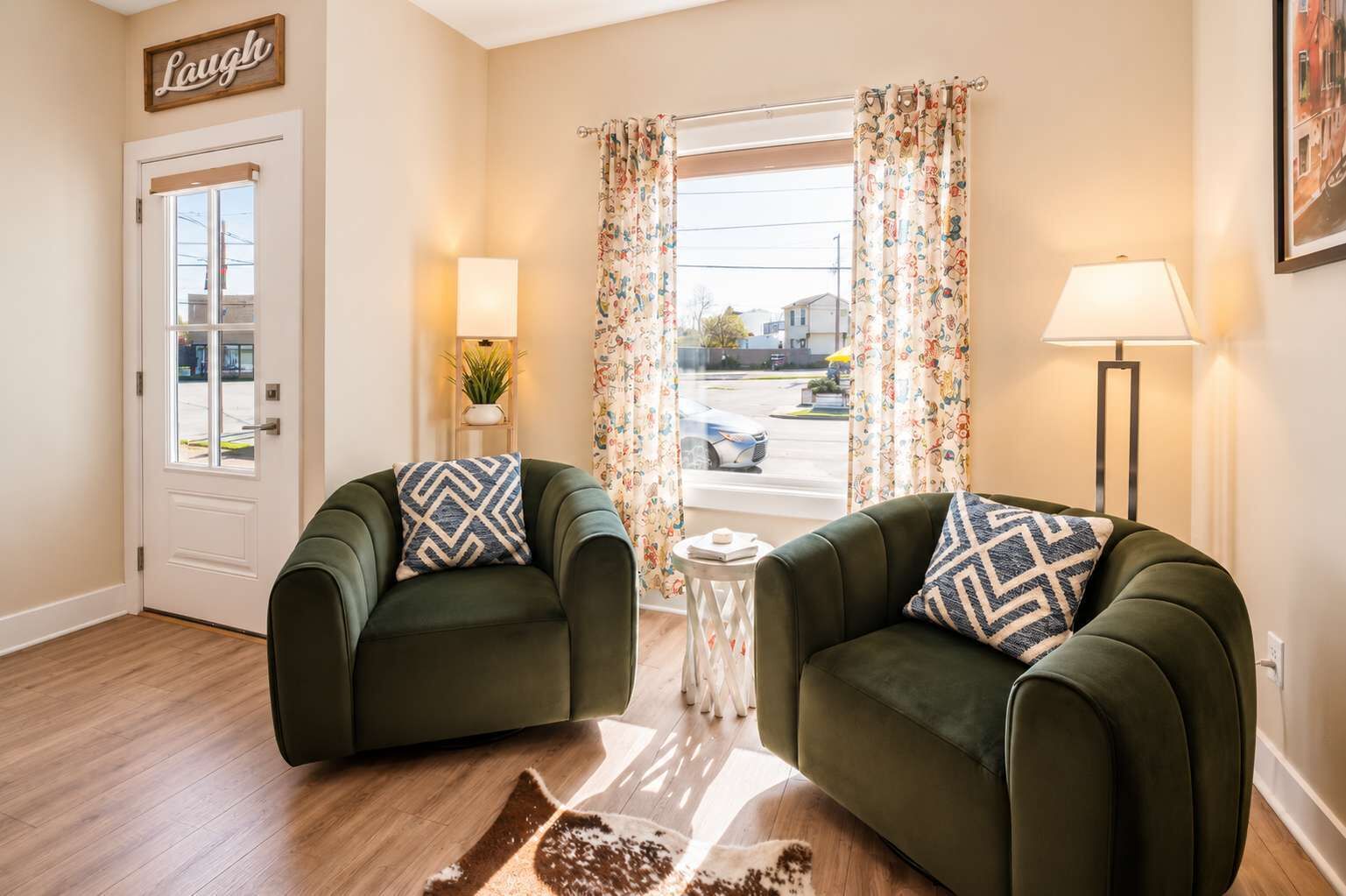 A room with two green armchairs, a small table with a plant, a lamp, and a door with a 'Laugh' sign.