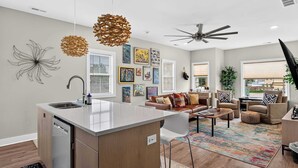 A modern kitchen with a central island, a dining area with a sofa and coffee table, and a living room with a couch and decorative pillows. - Cozy stay in Germantown near Downtown attractions! (Louisville)
