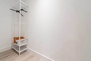 Ein weißes Regal mit Körben und Kleiderhaken vor einer schlichten Wand mit Holzboden.