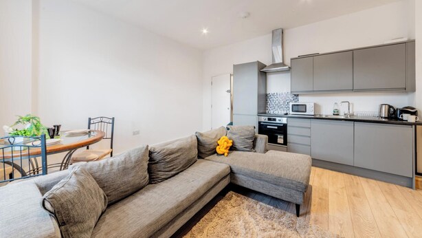 A modern apartment with a grey sofa, a dining table with chairs, a kitchen with grey cabinets, and a microwave. - Central - Stay 4 - Paid Parking - Near Transport (Maidstone)