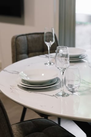 Une table à manger avec des assiettes et des verres à vin, une chaise, et une fenêtre en arrière-plan.