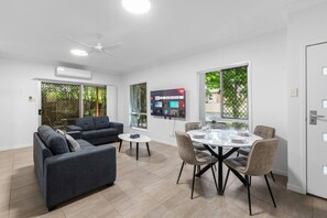 Un salon moderne avec un canapé, une table à manger pour quatre personnes et un téléviseur fixé au mur.