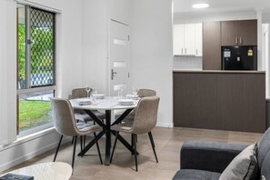 A dining area with a round table, four chairs, and a window with a view of greenery. - Peaceful Retreat Near Shops & Cafés|Secure Parking (Mount Warren Park)