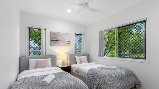 A room with two beds, a ceiling fan, a painting, and a window with a view of trees. - Peaceful Retreat Near Shops & Cafés|Secure Parking (Mount Warren Park)