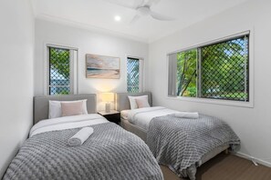 A room with two beds, a ceiling fan, a painting, and a window with a view of trees. - Peaceful Retreat Near Shops & Cafés|Secure Parking (Mount Warren Park)