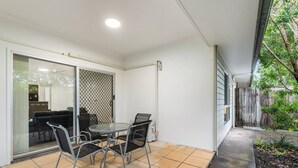 A patio with a round table and chairs, a sliding glass door, and a view of a backyard. - Peaceful Retreat Near Shops & Cafés|Secure Parking (Mount Warren Park)