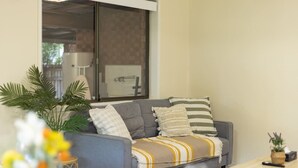 A living room with a sofa, a coffee table, a side table, and a potted plant.
