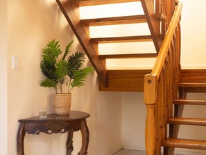 Un escalier en bois surmonté d’une verrière, une petite table avec une plante et un objet décoratif.