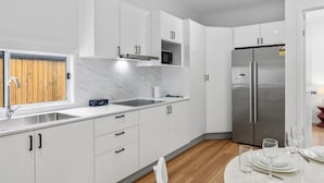 A modern kitchen with white cabinets, a stainless steel refrigerator, and a dining area with a table set for four.