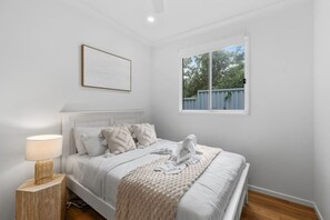 Een slaapkamer met een bed, een bedlampje, een raam en een ingelijste foto aan de muur.