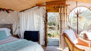 Une pièce confortable avec un lit, une chaise, une fenêtre avec des rideaux et une vue sur l’extérieur.
