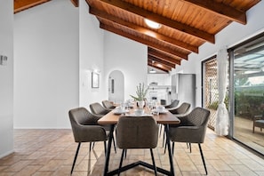 A dining area with a wooden table and chairs, a kitchen in the background, and a large sliding glass door leading to an outdoor area.