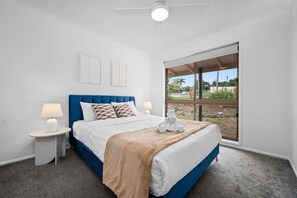 A bedroom with a bed, two bedside tables, a window, and a ceiling fan.