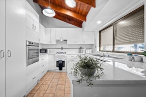 A modern kitchen with white cabinets, a built-in oven, a stove, a microwave, and a large window with blinds.