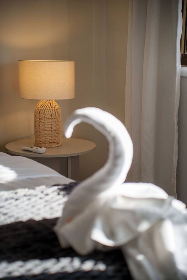 A bed with a white swan decoration, a lamp, and a small round table with a woven basket.