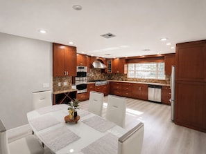 A modern kitchen with wooden cabinets, stainless steel appliances, and a dining area with a white table and chairs.