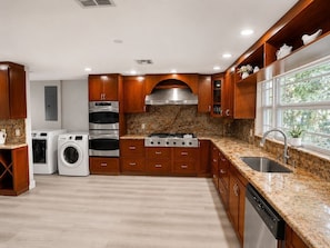 A modern kitchen with built-in appliances, wooden cabinets, granite countertops, and a window with a view.