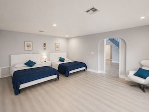 A modern bedroom with two beds, a white chair, and a staircase leading to another level.
