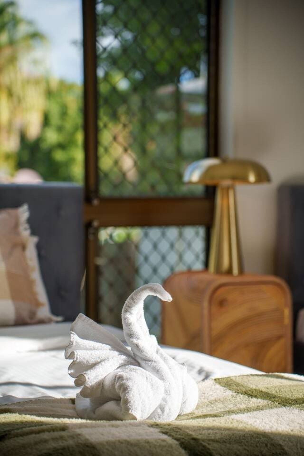 Ein handtuch in Schwanenform auf einem Bett mit Blick auf Grün hinter einem Fenster.