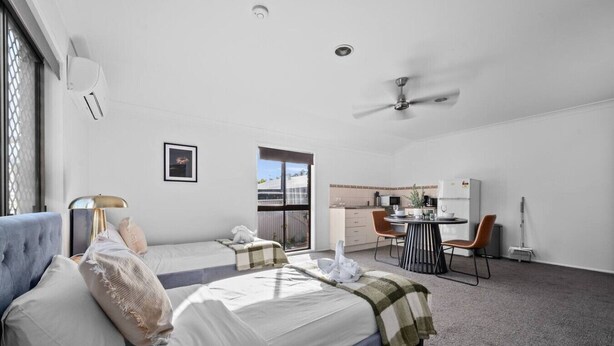 Une chambre d’hôtel avec deux lits, un bureau, une chaise, un ventilateur de plafond et une vue sur l’extérieur.