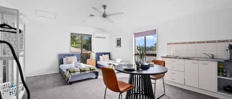 A modern hotel room with a dining area, two beds, a ceiling fan, and a view of the outdoors.
