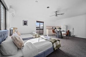 Ein Hotelzimmer mit zwei Betten, einem Schreibtisch, einem Stuhl, einem Deckenventilator und einem großen Fenster.