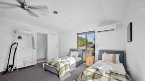 Une chambre avec deux lits, un ventilateur de plafond, une fenêtre et un coin buanderie.