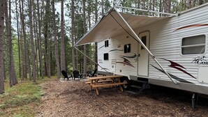 Ein Wohnmobil mit überdachter Terrasse, einem Picknicktisch und einer kleinen Holzterrasse.