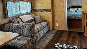 Ein gemütliches Wohnmobil-Interieur mit einer Sitzecke, einem Esstisch, einem gemusterten Teppich und einem Bett mit blumigem Bettzeug.