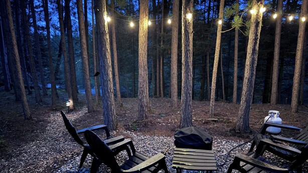 Ein Sitzbereich im Freien mit Stühlen und Tisch, umgeben von Bäumen und Lichterketten.
